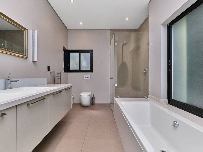 Modern bathroom featuring a floating vanity with double basins, a glass-enclosed shower, a built-in bathtub, and a wall-mounted toilet with neutral floor tiling.
