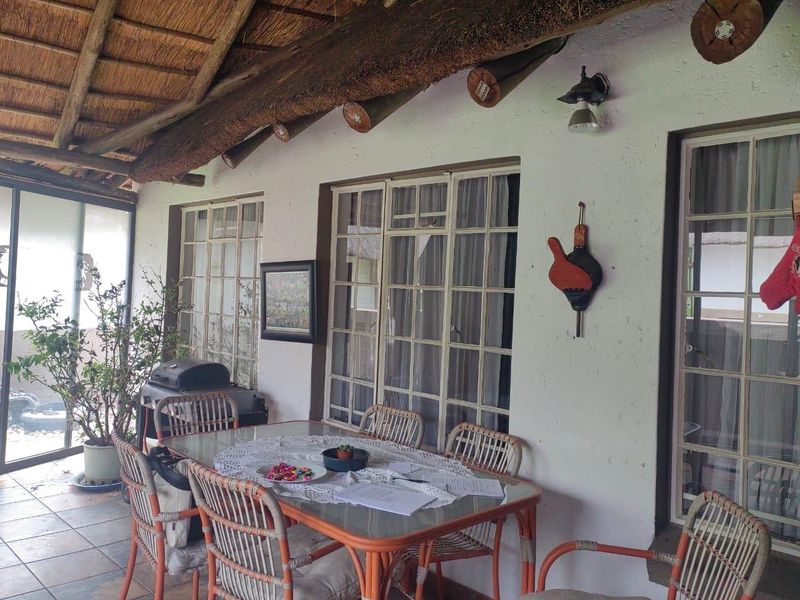 A covered patio area featuring a traditional thatched roof with exposed timber beams, tiled flooring, and steel-framed windows overlooking the garden.