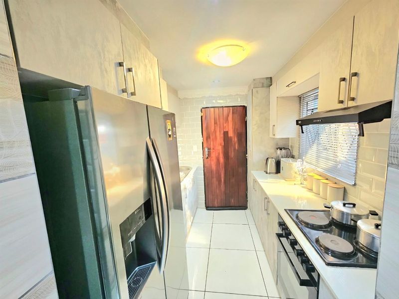 A functional galley-style kitchen featuring modern cabinetry, subway tile backsplash, built-in electric hob, oven, and extractor fan with tiled flooring.