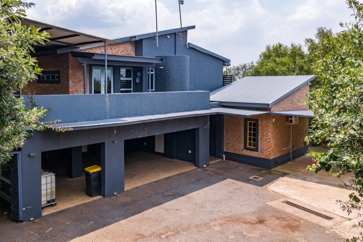 A view of the rear exterior of the house, featuring a covered parking area, brick and painted masonry walls, and a metal roof.