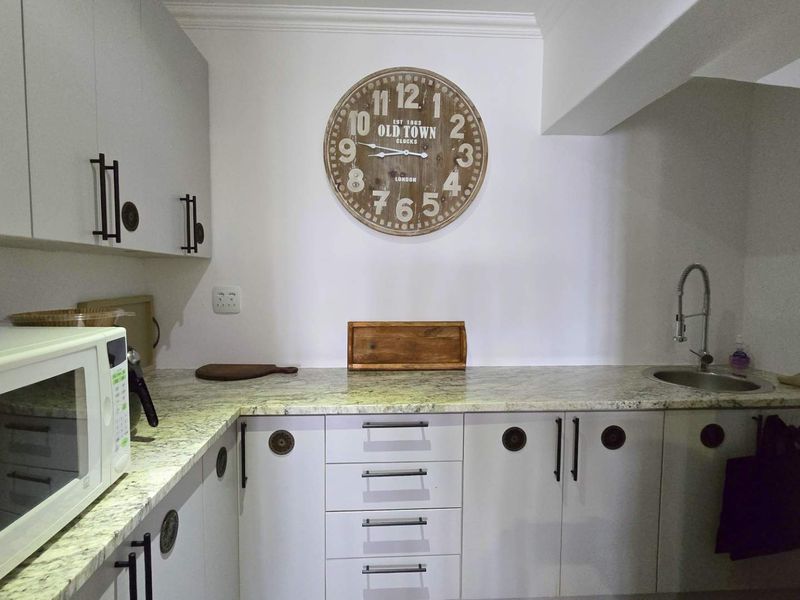A functional scullery area featuring light-toned cabinetry, granite countertops, an undermount sink with a gooseneck faucet, and ample storage space.