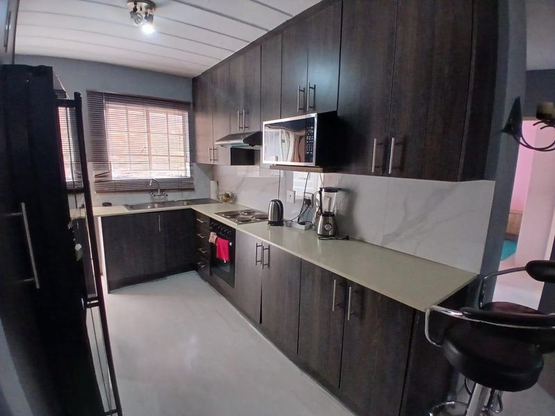 Modern kitchen featuring dark wood cabinetry, stone countertops, marble-look splashback, and integrated appliances including an oven, hob, and microwave.