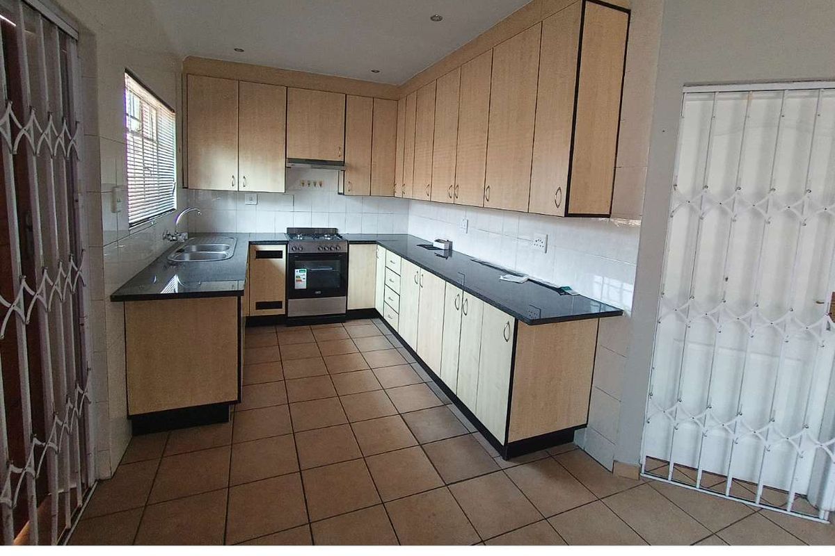Functional kitchen featuring light wood-finish cabinetry, dark granite countertops, tiled flooring, and a built-in stove with extractor fan.
