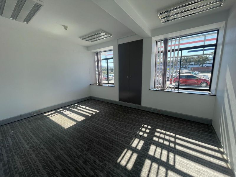 A bright, empty office space featuring carpeted flooring, recessed lighting, built-in storage, and large windows with vertical blinds.