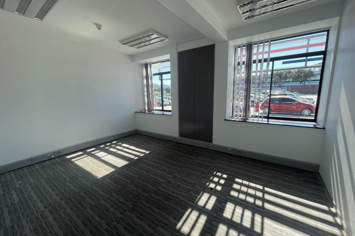 A bright, empty office space featuring carpeted flooring, recessed lighting, built-in storage, and large windows with vertical blinds.