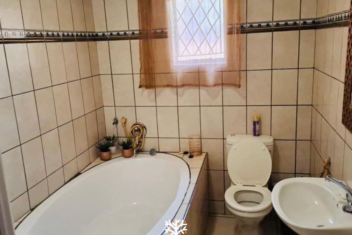 A functional bathroom featuring a built-in bathtub, a standard toilet, and a wall-mounted basin with full-height wall tiling.