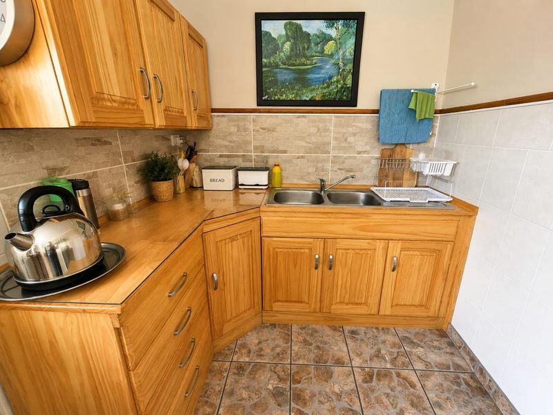 A functional kitchen area featuring wooden cabinetry, a double stainless steel sink, and stone-look tile finishes on the backsplash and floor.