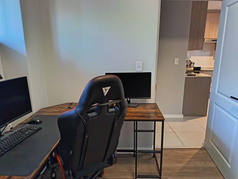A functional home office space featuring a mix of tiled and laminate flooring, with a view into the adjacent kitchen area.
