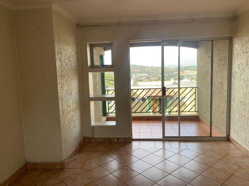 An empty living area featuring tiled floors, textured walls, and a sliding glass door providing access to a balcony with scenic views.