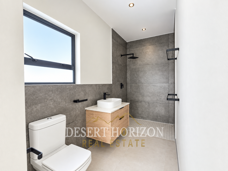 Modern bathroom featuring a walk-in shower, floating vanity with vessel sink, wall-mounted toilet, and contemporary grey tiling with black fixtures.