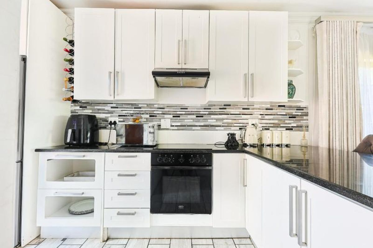 A modern kitchen featuring white cabinetry, black granite countertops, a built-in oven with extractor fan, and a decorative mosaic tile backsplash.