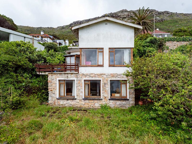 Rear elevation of a two-story house featuring stone cladding on the lower level, timber balcony, and large windows set against a mountain backdrop.