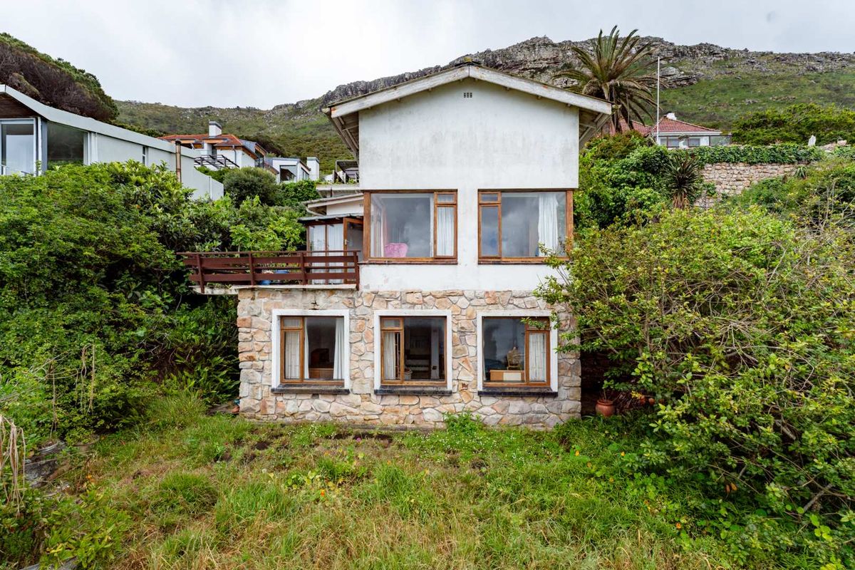 Rear elevation of a two-story house featuring stone cladding on the lower level, timber balcony, and large windows set against a mountain backdrop.