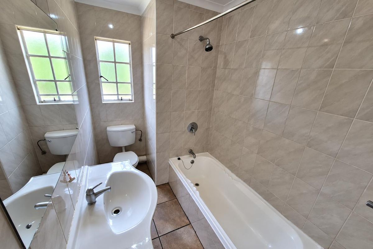 A functional bathroom featuring a built-in bathtub with shower, pedestal basin, and toilet, finished with neutral wall and floor tiling.