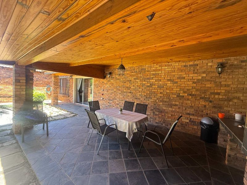 A covered patio area featuring a rustic exposed timber ceiling, brick walls, and slate tile flooring, providing a functional outdoor entertainment space.
