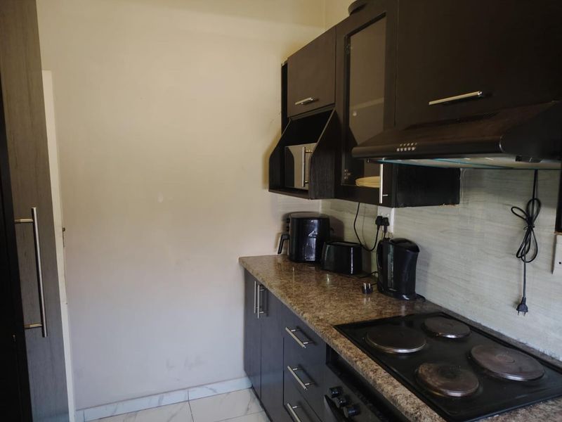 Compact kitchen featuring dark wood cabinetry, granite countertops, an integrated electric hob, and an extractor fan with tiled flooring.