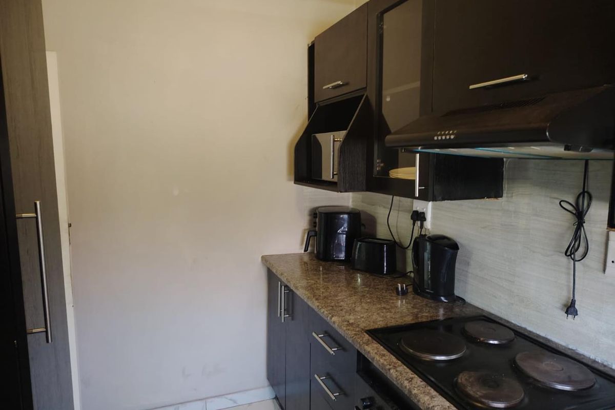 Compact kitchen featuring dark wood cabinetry, granite countertops, an integrated electric hob, and an extractor fan with tiled flooring.