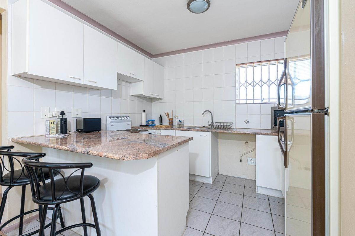 A functional kitchen featuring white cabinetry, granite-look countertops, tiled walls, and a breakfast bar area with tiled flooring.