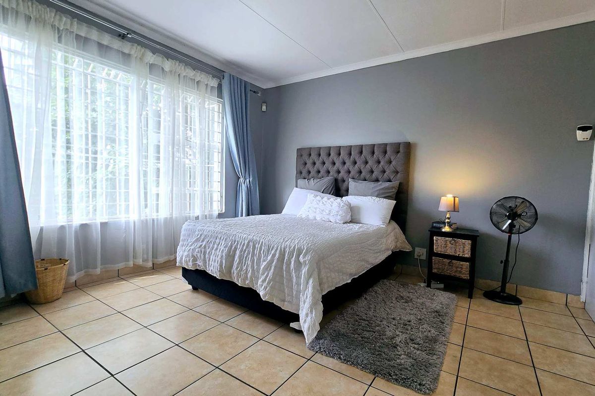A spacious bedroom featuring neutral grey walls, large windows with security bars, and durable tiled flooring.