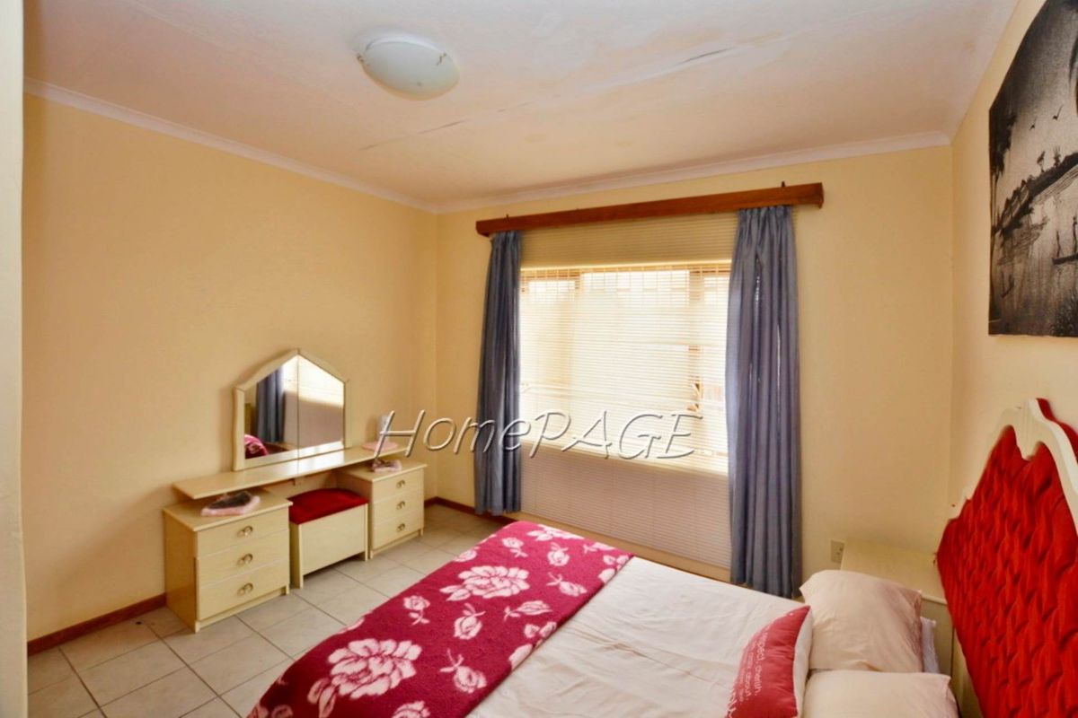 A standard bedroom featuring tiled flooring, a large window with fitted blinds, and a ceiling-mounted light fixture.