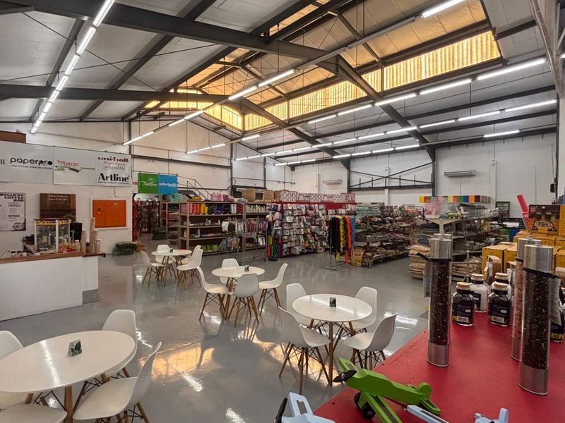 Spacious open-plan retail area featuring high ceilings with exposed steel trusses, abundant natural light from skylights, and durable epoxy-coated concrete flooring.