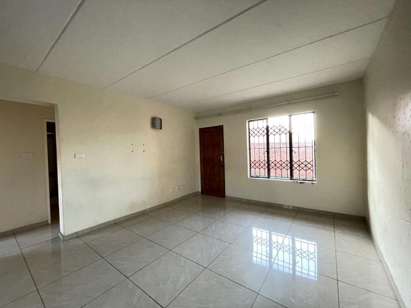 An empty living room featuring tiled flooring, a timber entrance door, and a window fitted with security bars.