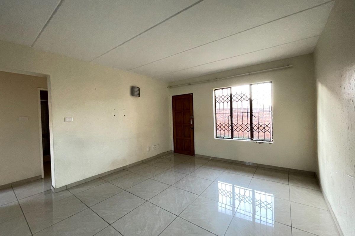 An empty living room featuring tiled flooring, a timber entrance door, and a window fitted with security bars.
