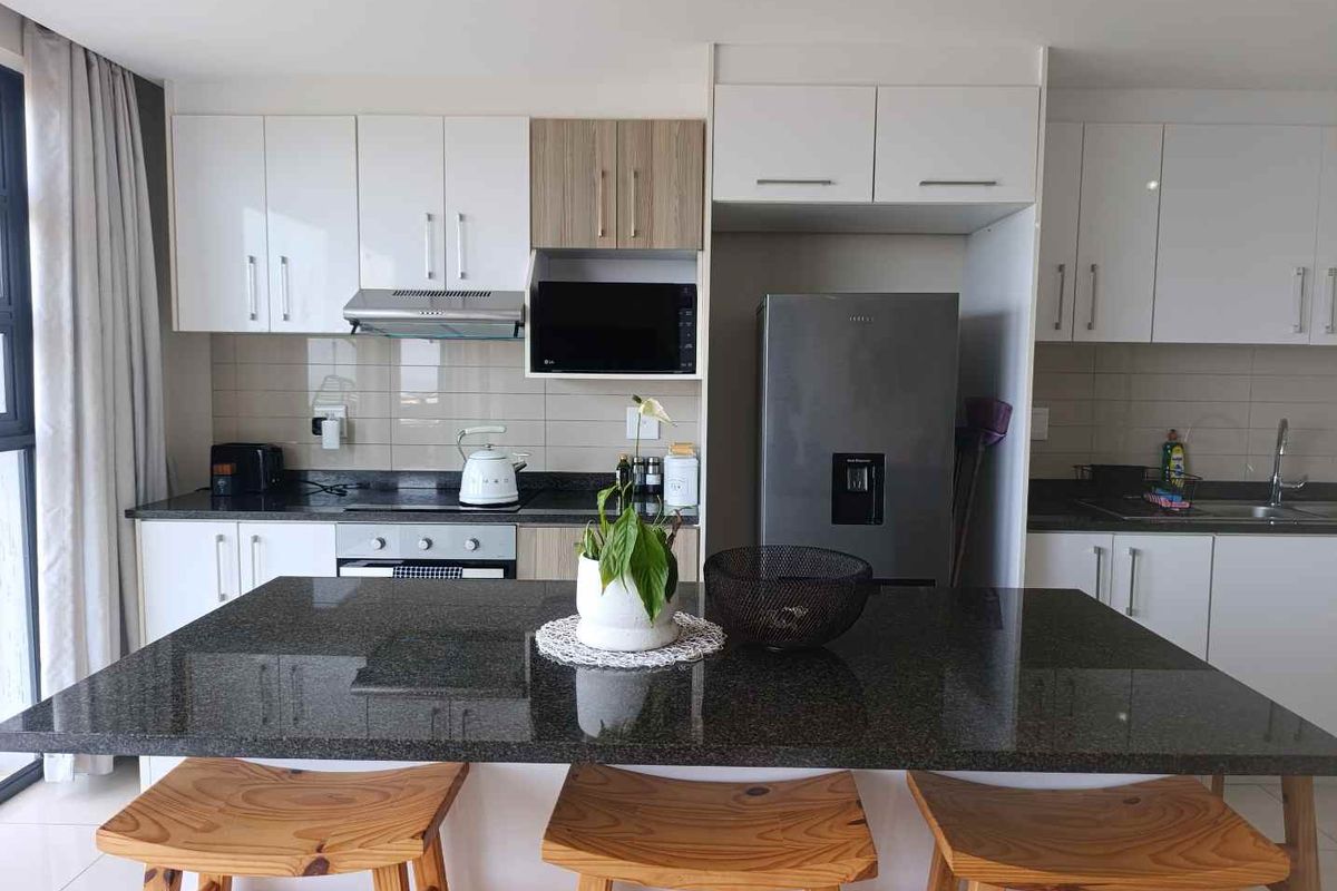 Modern kitchen featuring sleek white cabinetry, granite countertops, a central island, and integrated appliances, offering a clean and functional cooking space.