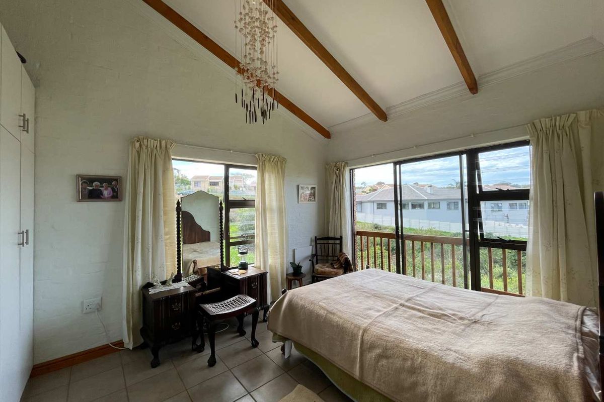 Spacious bedroom featuring a vaulted ceiling with exposed timber beams, tiled flooring, built-in wardrobe, and sliding glass doors opening to a balcony.