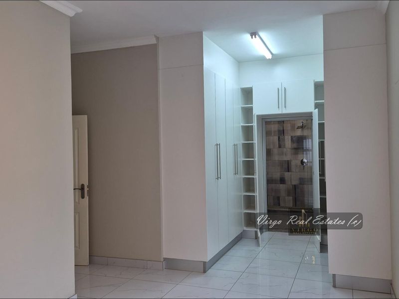 A clean, empty bedroom featuring modern white built-in cupboards, tiled flooring, and direct access to an en-suite bathroom.