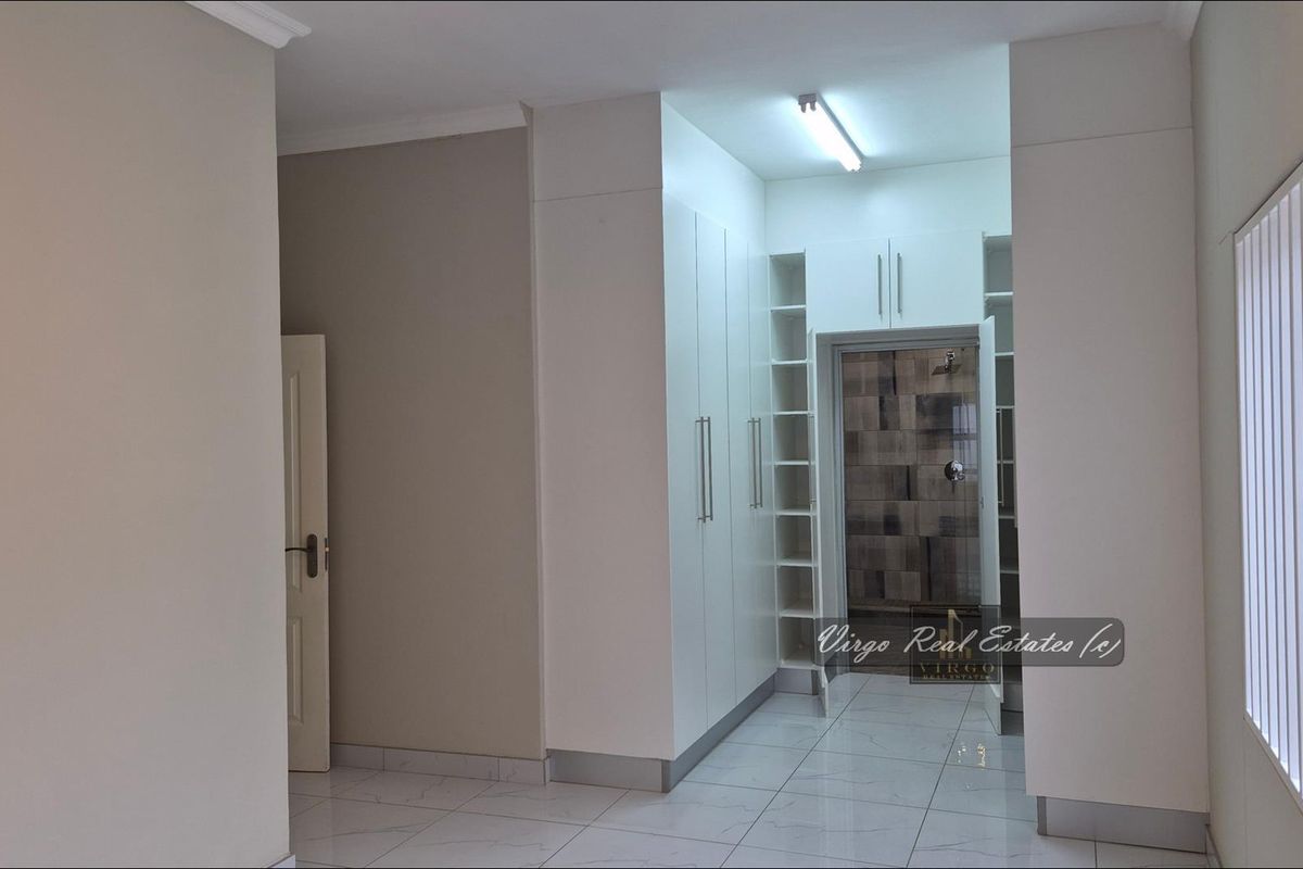 A clean, empty bedroom featuring modern white built-in cupboards, tiled flooring, and direct access to an en-suite bathroom.