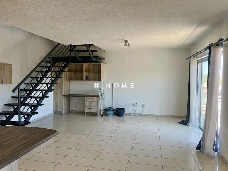 Open plan living area featuring a modern metal staircase, built-in desk with shelving, tiled flooring, and access to a balcony through sliding glass doors.