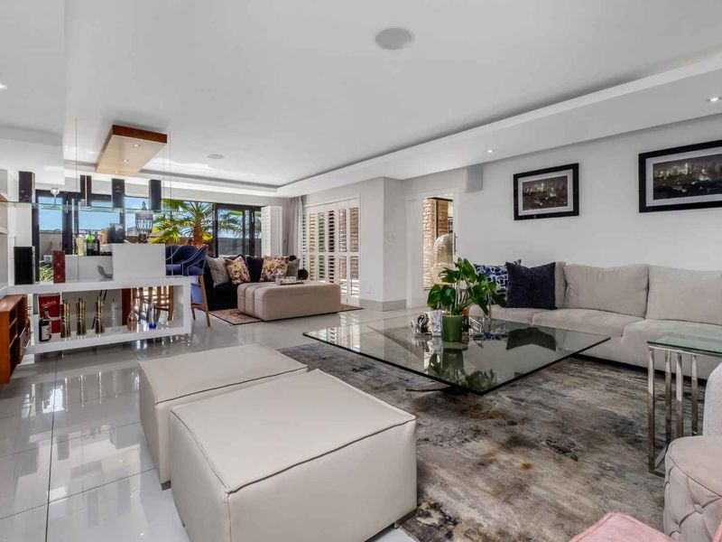 Spacious open-plan living area featuring polished porcelain tiles, recessed lighting, and a built-in bar, seamlessly connecting to the outdoor patio through sliding glass doors.