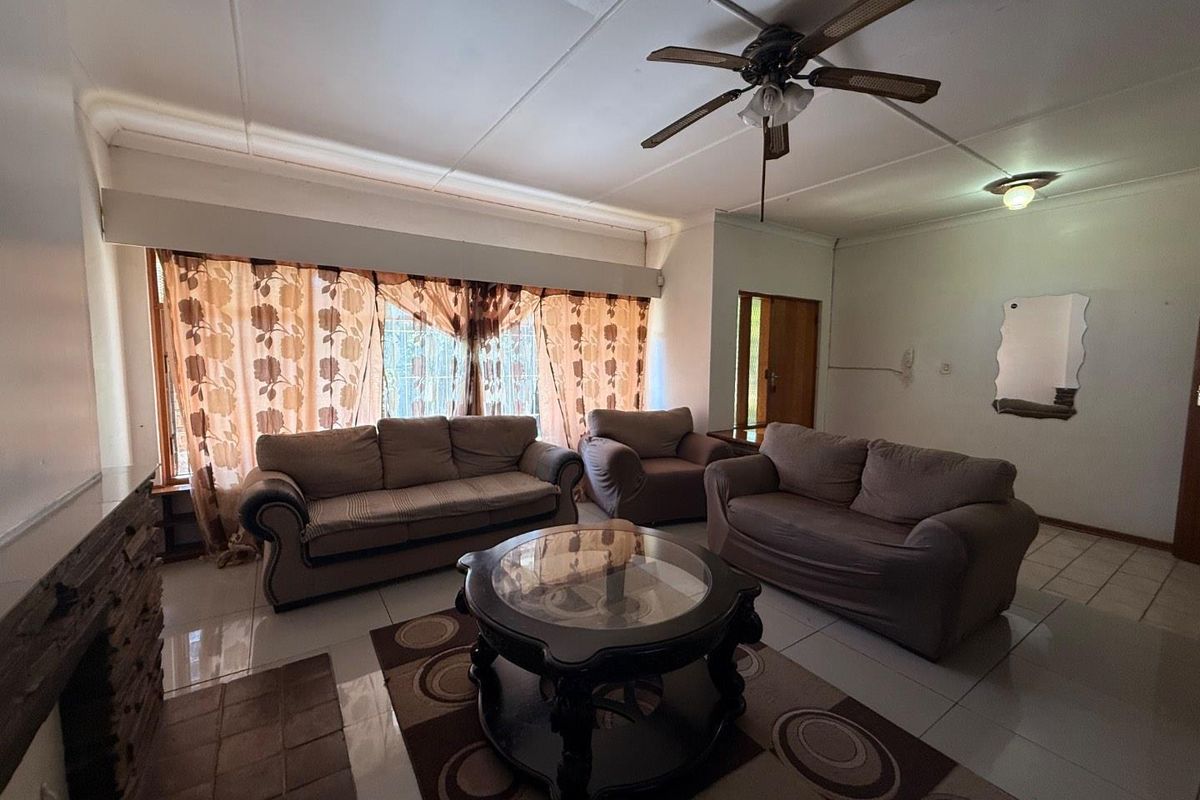 A spacious living room featuring tiled flooring, a ceiling fan, and large windows that provide natural light.