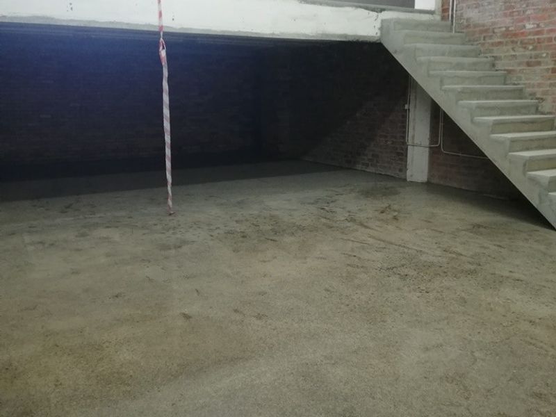 An expansive, industrial-style open plan space featuring exposed brick walls, a concrete staircase, and a mezzanine level, currently in a shell condition.