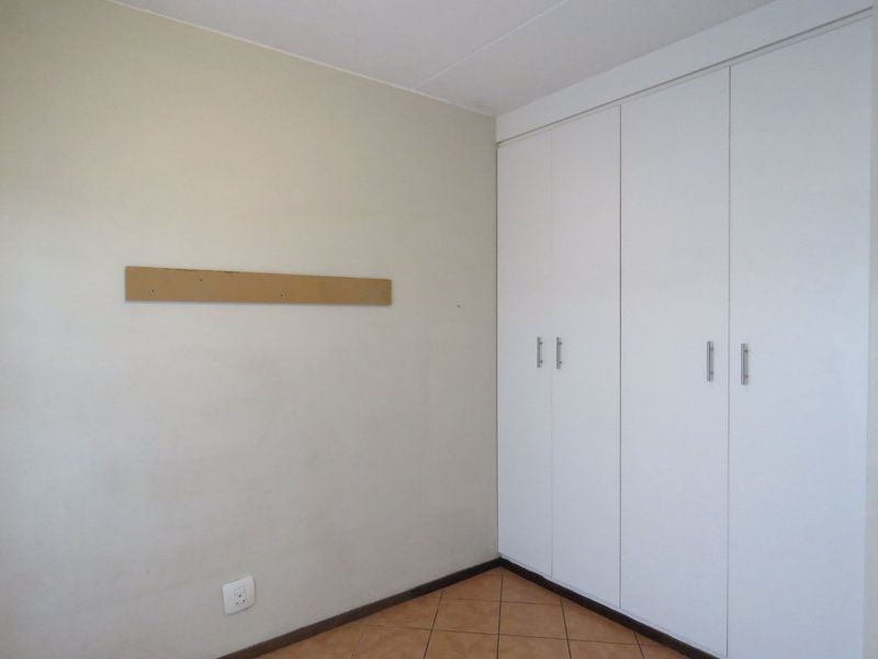 A clean, empty bedroom featuring built-in white cupboards, tiled flooring, and neutral wall finishes, ready for personalization.