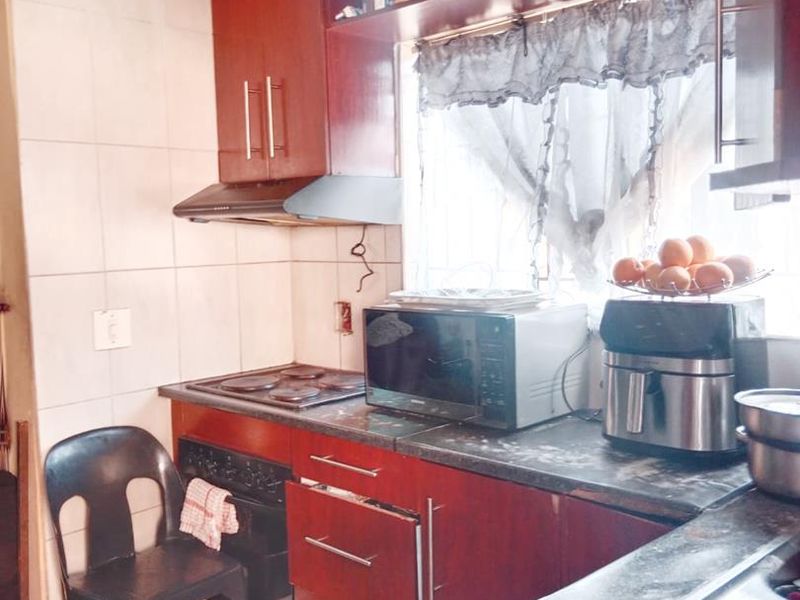 A compact kitchen featuring dark wood cabinetry, an electric hob, built-in oven, extractor fan, and a stainless steel sink with tiled splashbacks.