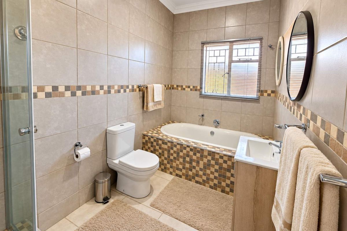 A well-maintained bathroom featuring a built-in bathtub, separate shower enclosure, vanity basin, and neutral tiled finishes with decorative mosaic accents.