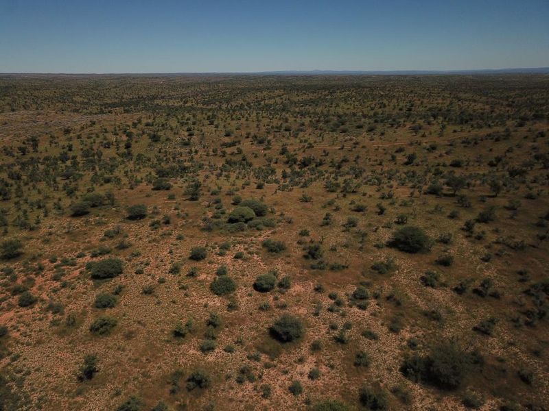 An aerial view of expansive, undeveloped residential land featuring natural terrain and native vegetation under a clear sky.