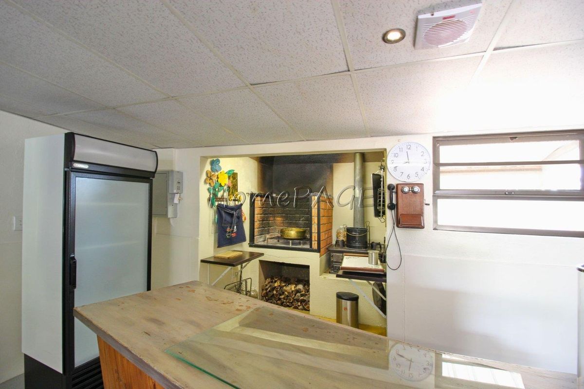 Indoor entertainment area featuring a built-in brick braai fireplace, tiled ceiling, and functional prep space.