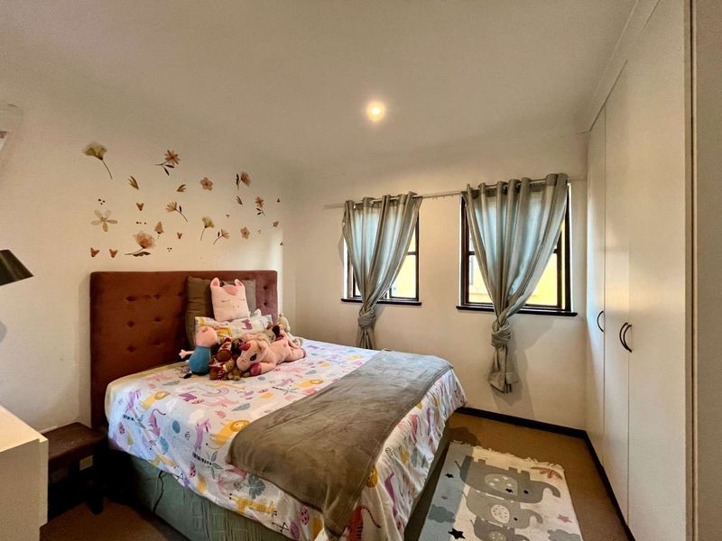 A well-maintained bedroom featuring built-in cupboards, recessed downlighting, and dual windows providing natural light.