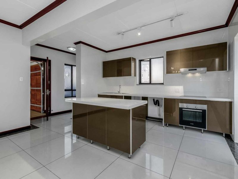 Modern kitchen featuring a central island, glossy cabinetry, built-in oven, electric cooktop, and sleek tiled flooring in a bright, open-plan layout.