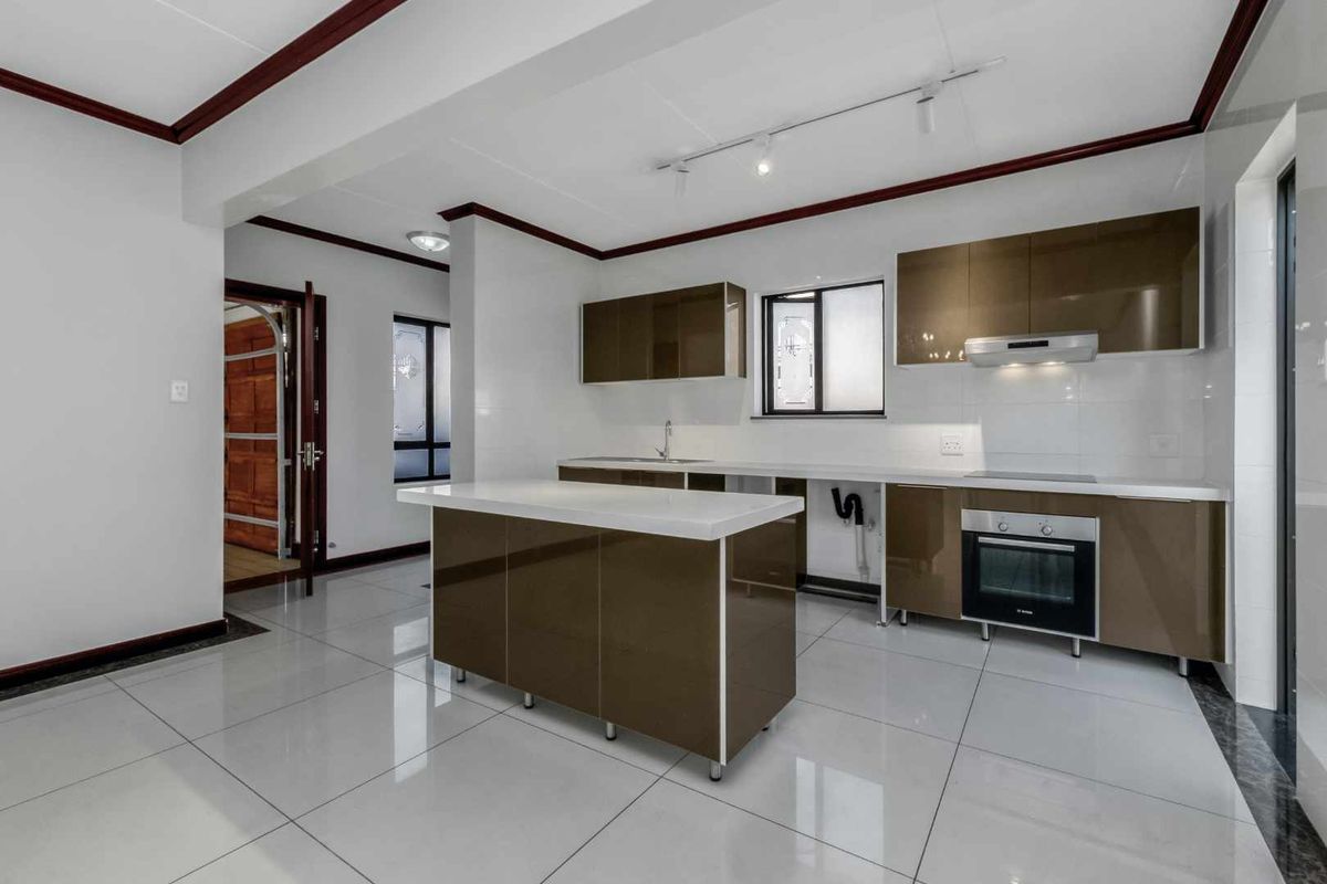 Modern kitchen featuring a central island, glossy cabinetry, built-in oven, electric cooktop, and sleek tiled flooring in a bright, open-plan layout.