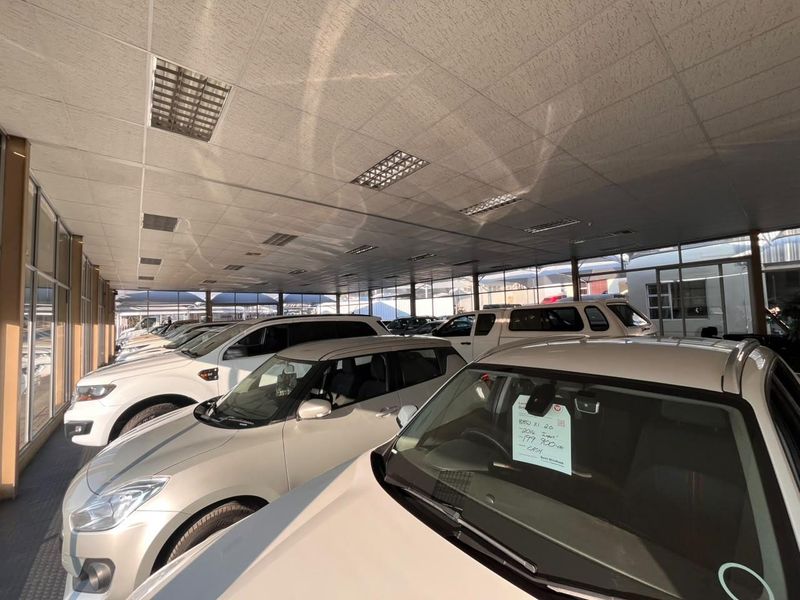 A spacious commercial showroom or garage area featuring a suspended ceiling with recessed lighting and extensive glass frontage for vehicle display.