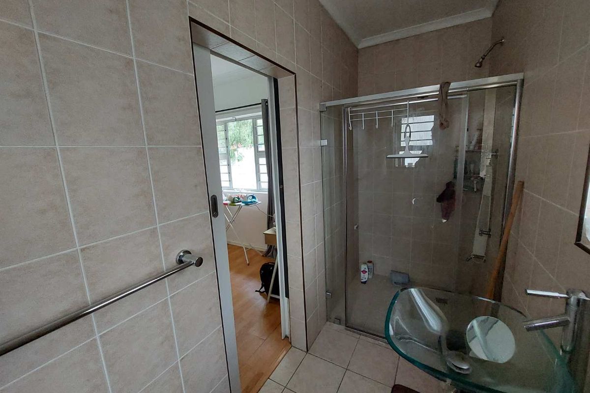 A functional bathroom featuring a glass shower enclosure, tiled walls, and a modern glass basin, with a doorway leading to an adjacent room.