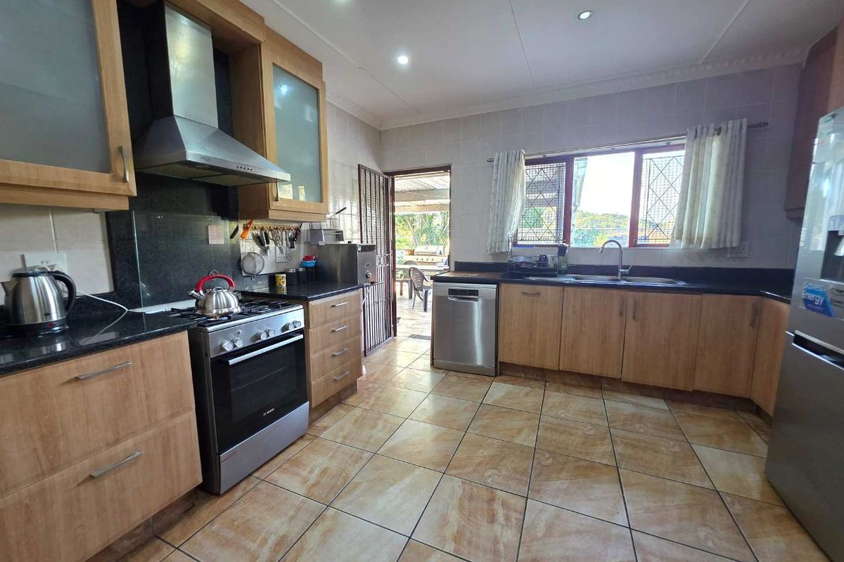 A functional kitchen featuring wood-look cabinetry, granite countertops, a stainless steel extractor fan, and direct access to an outdoor patio area.
