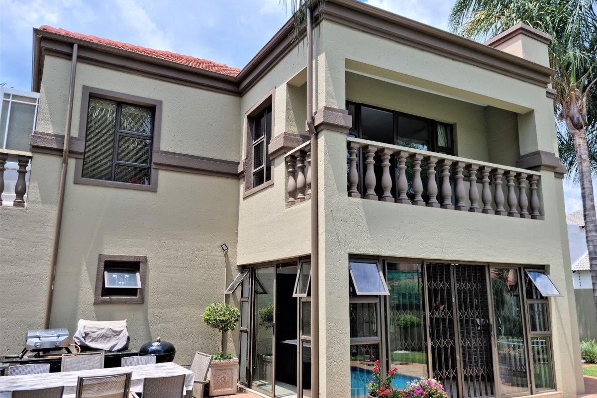 Rear elevation of a double-story house featuring a covered balcony with balustrades, ground-floor patio, and sliding doors leading to the garden and pool area.
