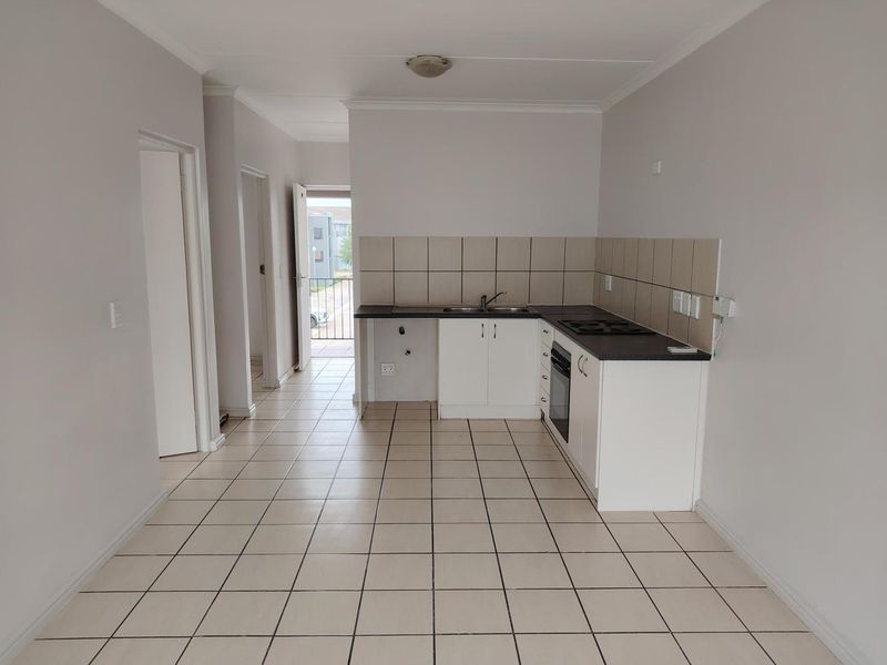 A functional, empty kitchen featuring white cabinetry, dark laminate countertops, built-in oven, electric hob, and neutral ceramic floor tiles.