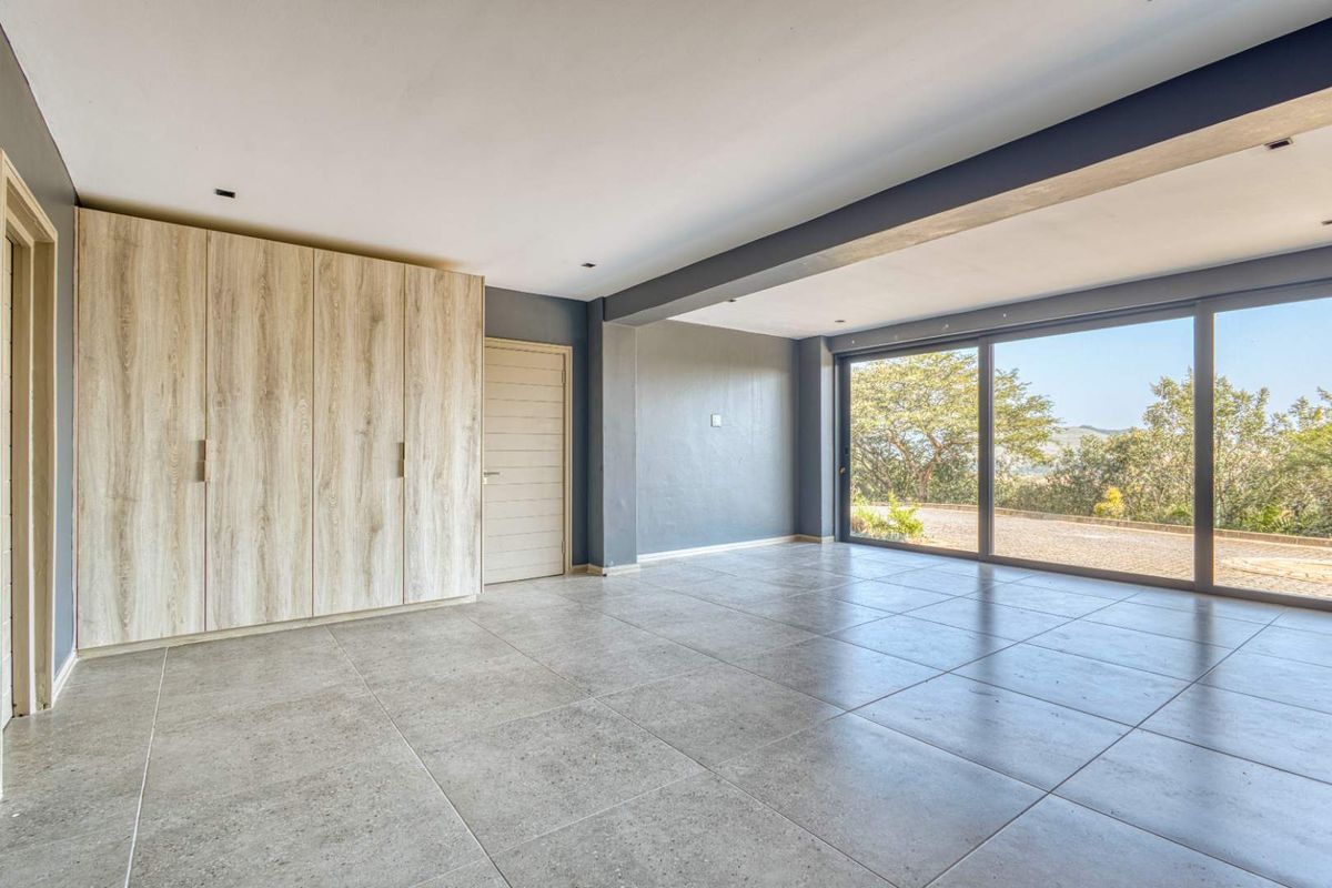 Spacious bedroom featuring large sliding glass doors, neutral tiled flooring, and modern built-in cupboards with a clean, contemporary finish.