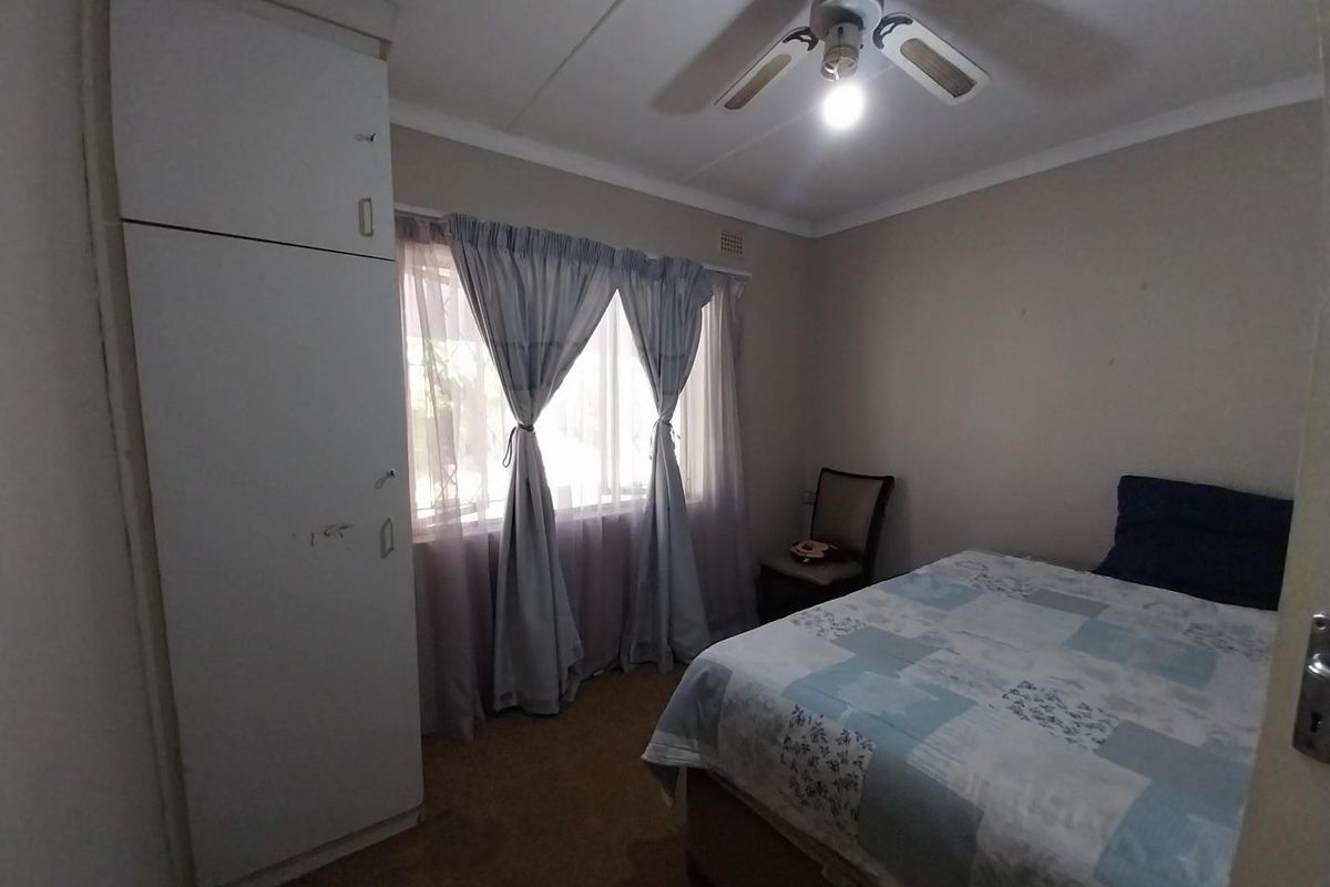 A bedroom featuring a built-in wardrobe and a ceiling fan, with neutral wall tones and a window providing natural light.